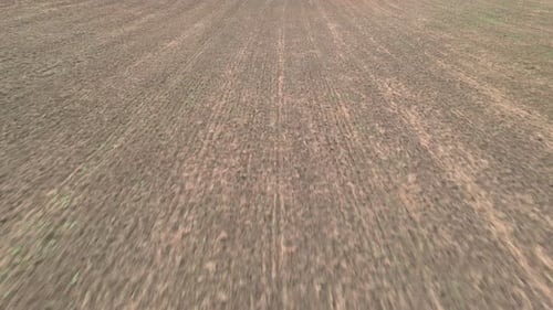 Flying over a plowed field with little vegetation