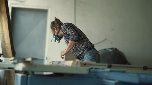 Carpenter with Respirator Mask Cutting Wood on Table Saw