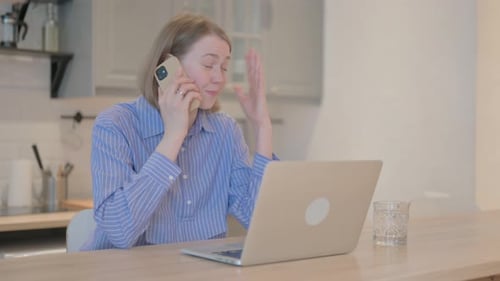 Woman Talking on Phone at Laptop Indoors