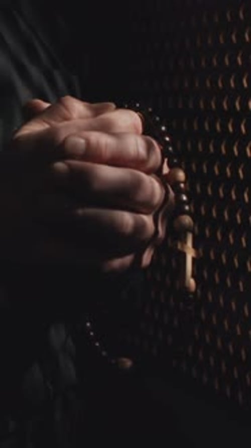 Person Holding Rosary Prayer Beads in Dark Setting