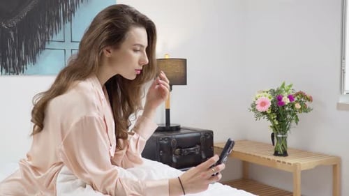 Young Woman Looks at Phone on Bed