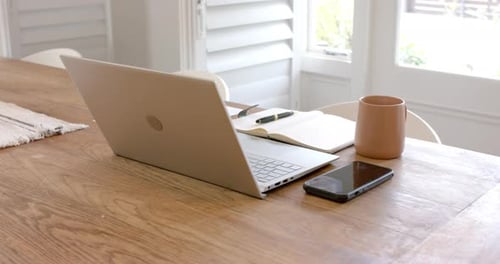 Laptop, smartphone, notebook, and coffee mug on wooden table in home office