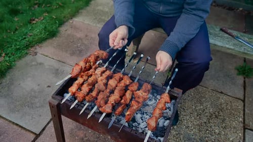 Grilled Meat Skewers Sizzling on Barbecue Over Hot Coals Hands Turning Kebabs on Metal Skewers to