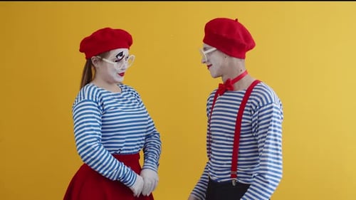 Ein männlicher Pantime und eine weibliche Pantomime in gestreiften und hellen Anzügen lächeln und umarmen sich fest