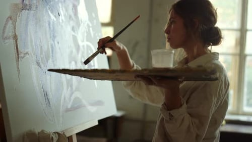 Silhouette of Young Woman Artist Painting on Canvas in Modern Studio. Tired