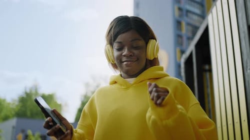 Portrait Of African American Woman With Smartphone Walking And Listening To Music By Headphones