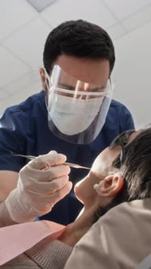 Vertical of Dentist in Protective Scrubs Using Sterile Instruments on Patient