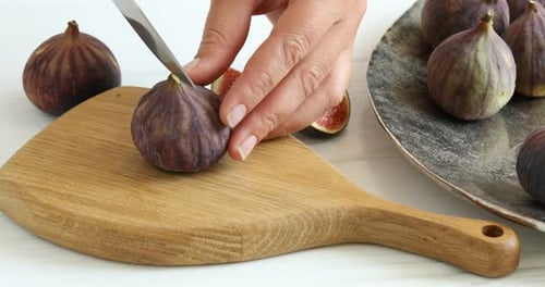 Mujer cortando higos maduros en una mesa blanca, primer plano