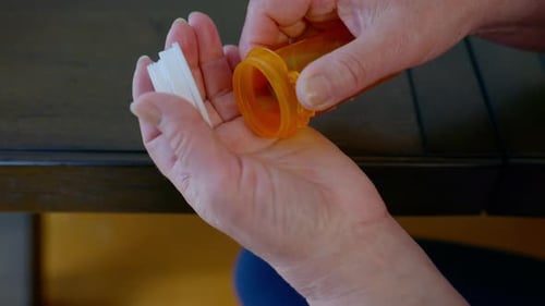 Close Up Footage of Elderly Hands Pouring Pills From an Orange Prescription Bottle Into the Palm