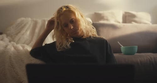 Sad Blonde Girl in a Black Tshirt Slumped on Her Hand and Watches a Boring Movie Near the Sofa at