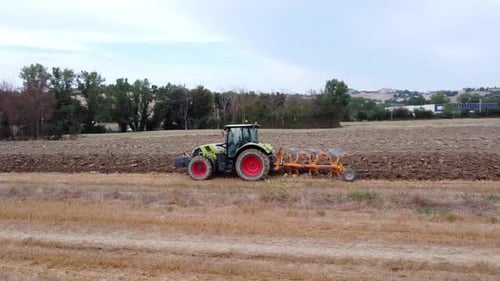 aerial view of a soil plowing tractor on a large farm on a cloudy day, orbit wide shot