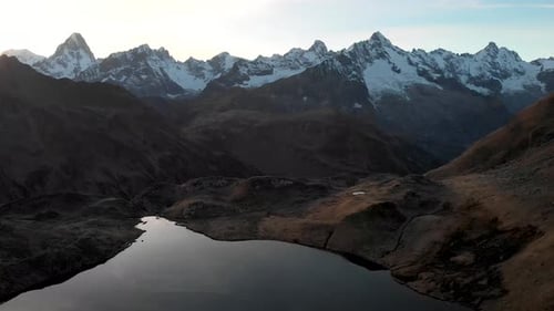 Aerial flyover over the shores of a half frozen lake during autumnn sunset in the Alps