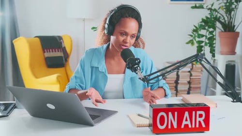 Jovem blogueira afro-americana sociável se senta à mesa com microfone