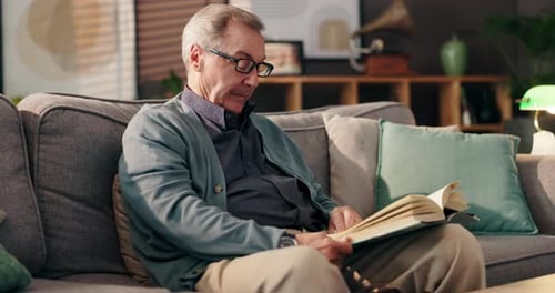 Senior Man Reads a Book on the Couch