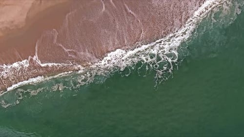 View From an Aerial Perspective of Waves Crashing Against a Sandy Shoreline on Surface of Ocean