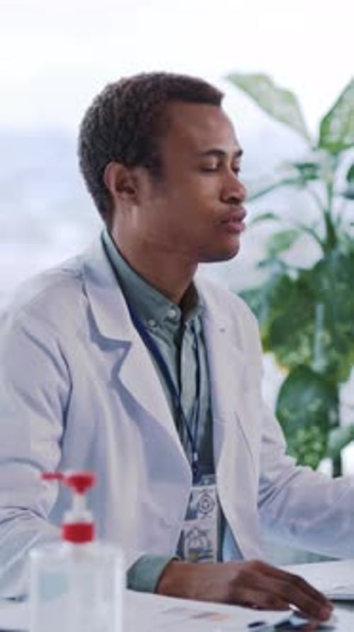 A Doctor in a Lab Coat Works Focused at His Desk with a Laptop