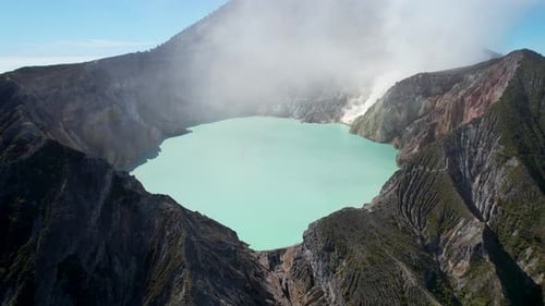 Aerial Closeup of the rim of a steaming volcano Ijen with a Turquoise Lake, and foggy cloudy Mountai