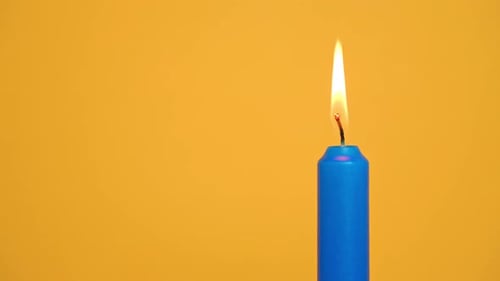 Single bright blue candle burn on a yellow background.