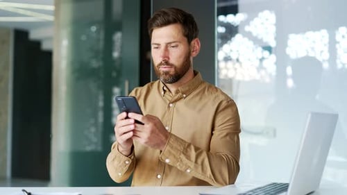 Businessman is using smartphone while sitting at workplace in business office. Worker reads