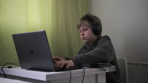 Junge spielt aufmerksam Computerspiele mit Kopfhörern, Maus und Gaming-Tastatur am heimischen Schreibtisch