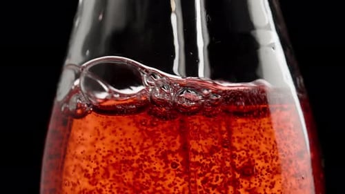 Macro Bottle with Red Soda, Inserting a Straw Inside and Blowing, Bubbles Rising in Slow Motion.