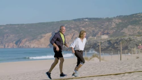 Smiling Mature Man and Woman Running on Beach on Summer Day