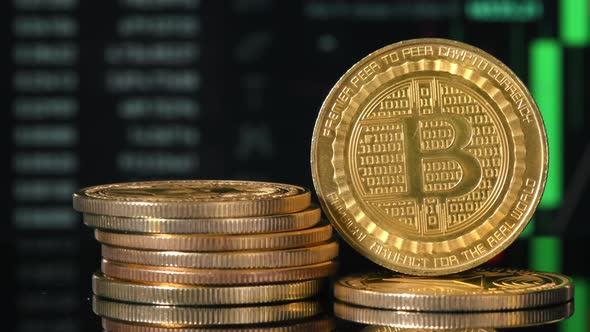 Close view of multiple physical Bitcoins with moving digital charts ...