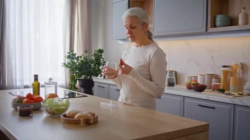 Senior Woman Taking Pill with Water in Kitchen