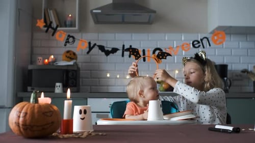 Girl Puts Halloween Headband on Toddler in Kitchen