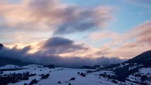 Winterlicher Berg-Zeitraffer mit Wolken, die sich bei Sonnenuntergang über schneebedeckte Gipfel und Wälder wälzen