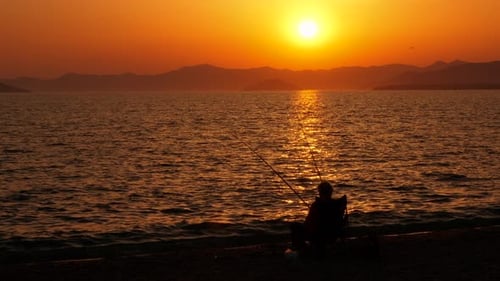 Fischer-Silhouette sitzt am See in der Abenddämmerung
