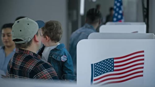 Caucasian Man with Kid on Hands Stands at Voting Booth