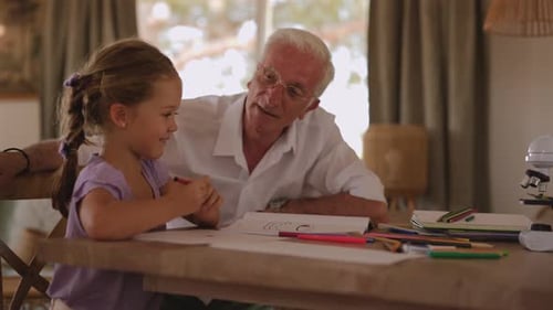 Caring grandfather helping his happy granddaughter with her drawing, sharing a warm and loving momen