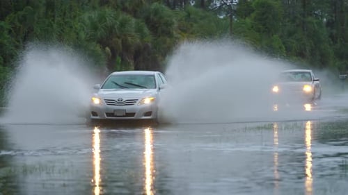 Flooded American Street with Moving Vehicles Surrounded with Water in Florida Residential Area