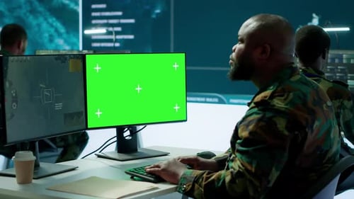 Military Specialist Monitors Satellite Data Next to Green Screen Display