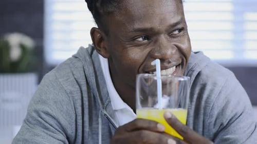 Man Drinks Orange Juice With a Straw Indoors