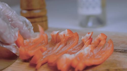 Front View of the Young Chef Cut Thin Slices of a Piece of Red Pepper with a Knife on the Cutting