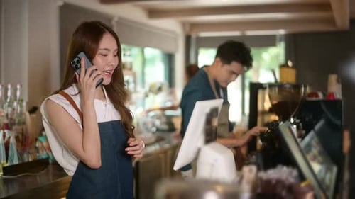 Young Asian service minded barista with customer in coffee shop