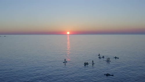 Group of paddle boarders on the water at sunset watching the sun set below the horizon.
