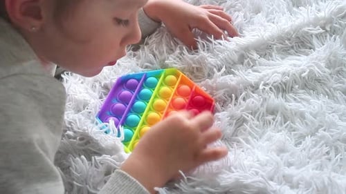 Kid playing with pop it sensory toy. girl pressing on colorful rainbow squishy soft silicone bubbles