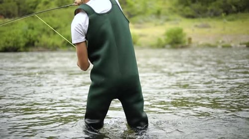 Shot of a Caucasian male fisherman casting his hook while Fly Fishing. He is standing in the middle