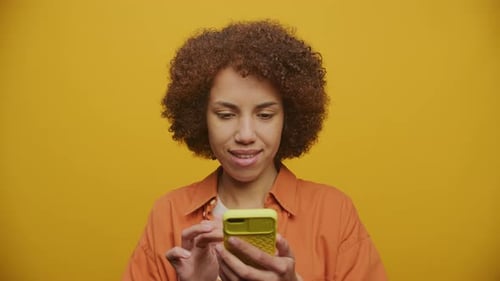 Young Adult Scrolls Phone on Yellow Background