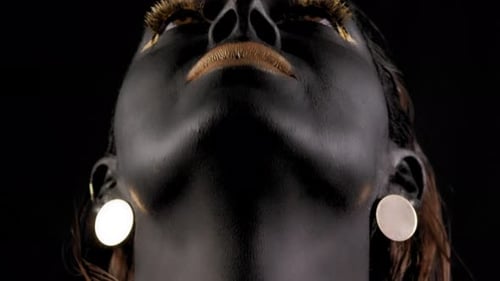 A Woman's Face with Black Skin Golden Lips Long Golden Eyelashes in a Studio