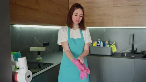 Woman Puts on Gloves in Kitchen to Clean