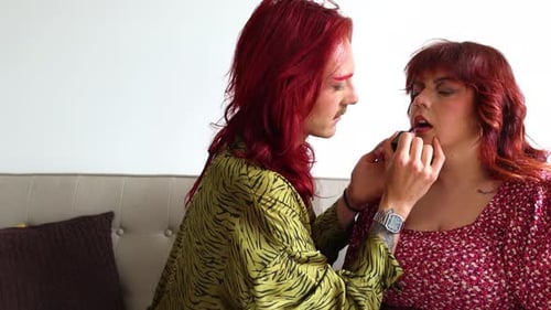 Non-binary person applying lipstick on their friend's lips