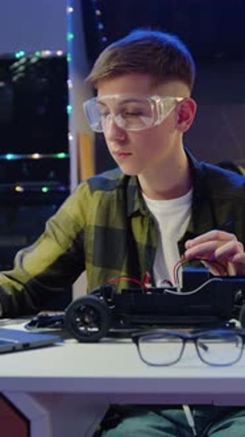 Teen Building a Robot Car at Home at Night