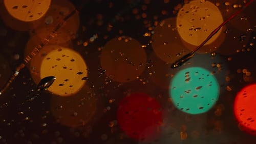 Water drops flowing down windshield of car at night defocus bokeh. Rainy night city lights bokeh