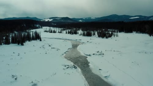 Aerial view of snow white bank of a winter meandering stream. Mountains of Creek