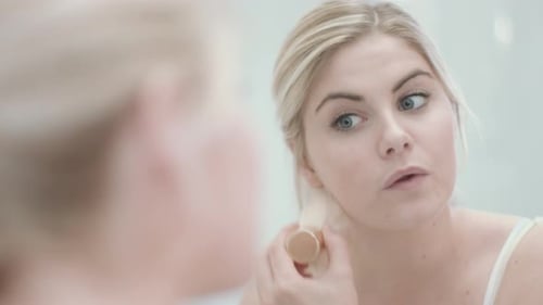 Woman Applying Makeup with Brush in Home Bathroom