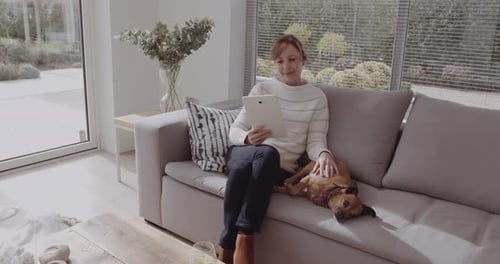 Woman Relaxing on Sofa with Dog, Using Tablet